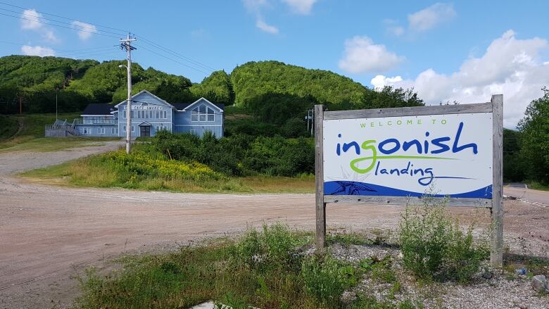 A wood-framed sign says Welcome to Ingonish Landing with a ski lodge in the background among trees on the side of a hill.