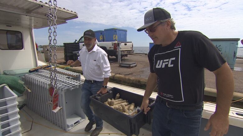 Two men carrying a plastic tub filled with bait sausages onto a fishing boat