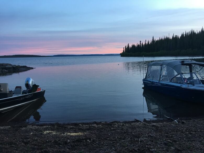 Boats are seen beached on the shore of a large lake in twilight.