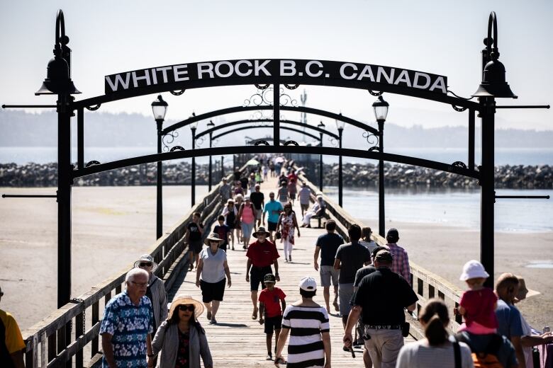 A series of people walk down a long pier. A sign reads 'White Rock B.C. Canada'