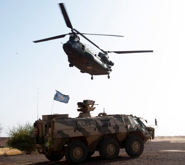 A large helicopter flies over a tank.