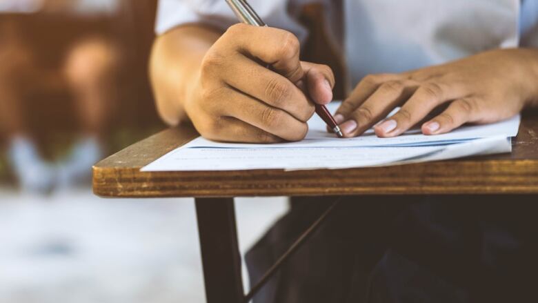 A close-up photo of someone with a pen writing on paper on a desk.