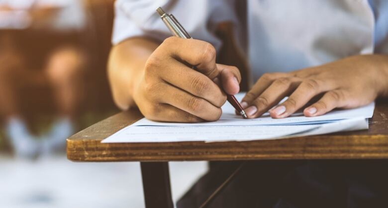 A close-up photo of someone with a pen writing on paper on a desk.