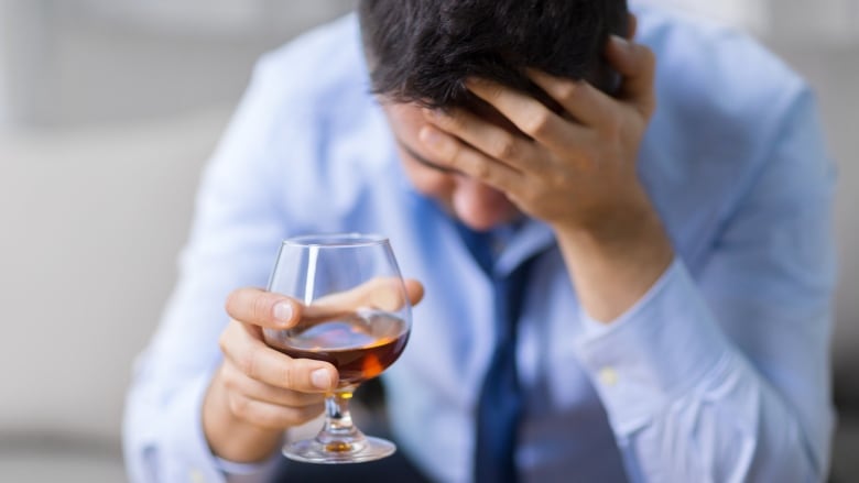 A man looks sad, holding a glass of wine.