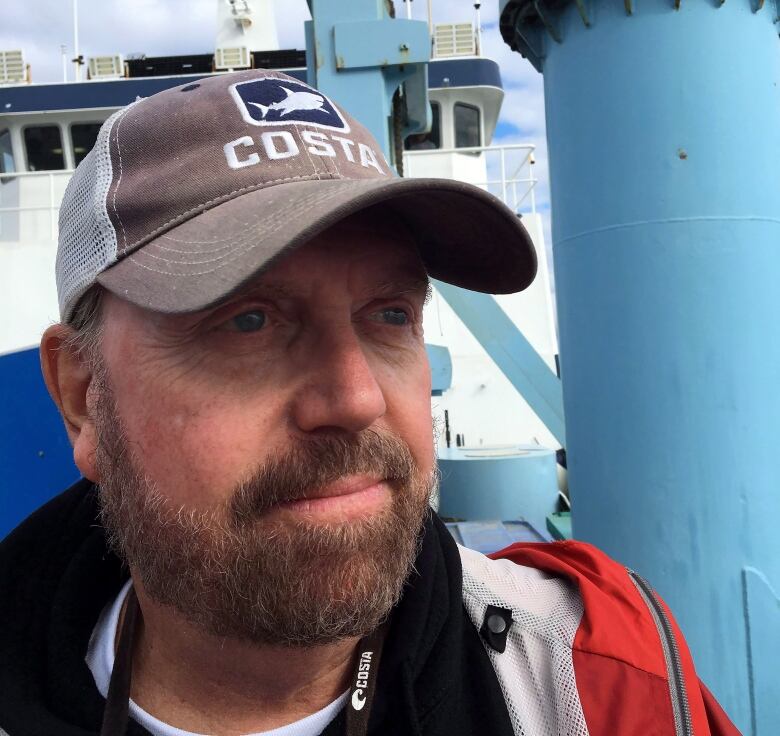 Man with beard wearing baseball hat, on board a ship.