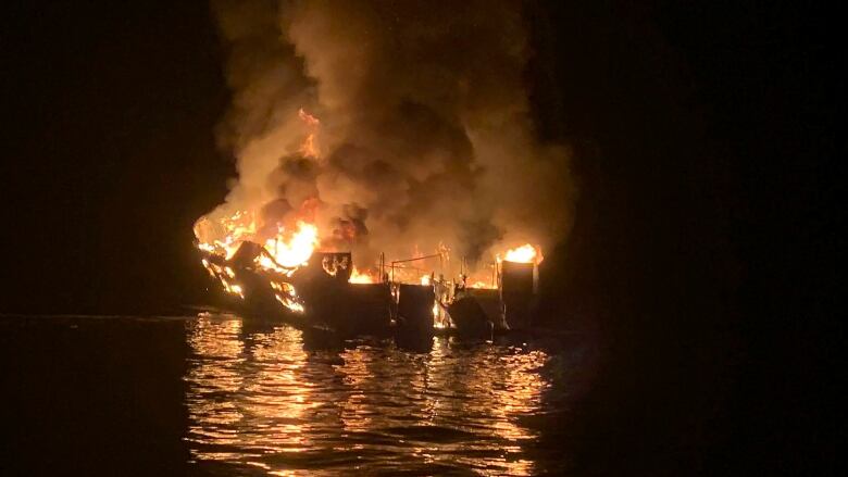 A boat burns on the water at night.