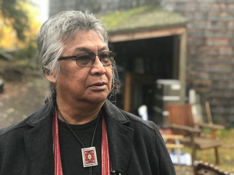 Portrait of a man with grey hair and glasses, standing outside.