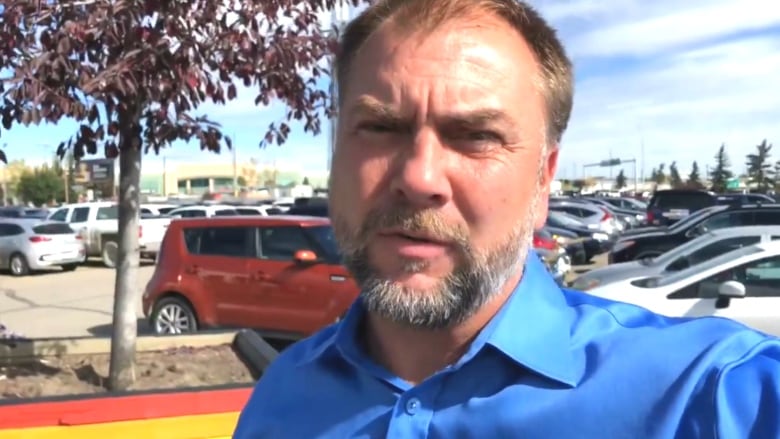 A man in a blue shirt appears to be recording himself in a parking lot.