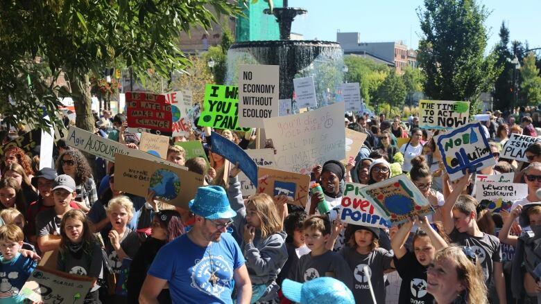 Many people gather together outdoors hold signs about the climate. They are in front of the Gore Park fountain.