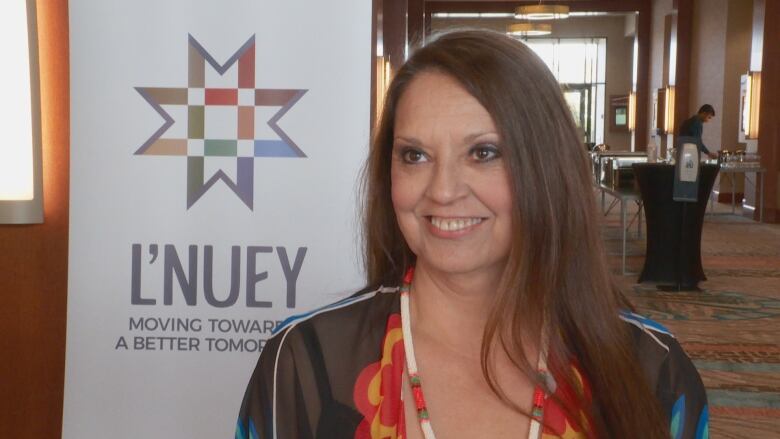 A woman with long brown hair stands by a poster that says 