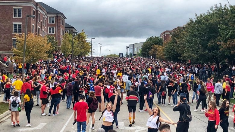 Young people wearing red and black (University of Guelph athletics colours) gather by the hundreds on a residential street