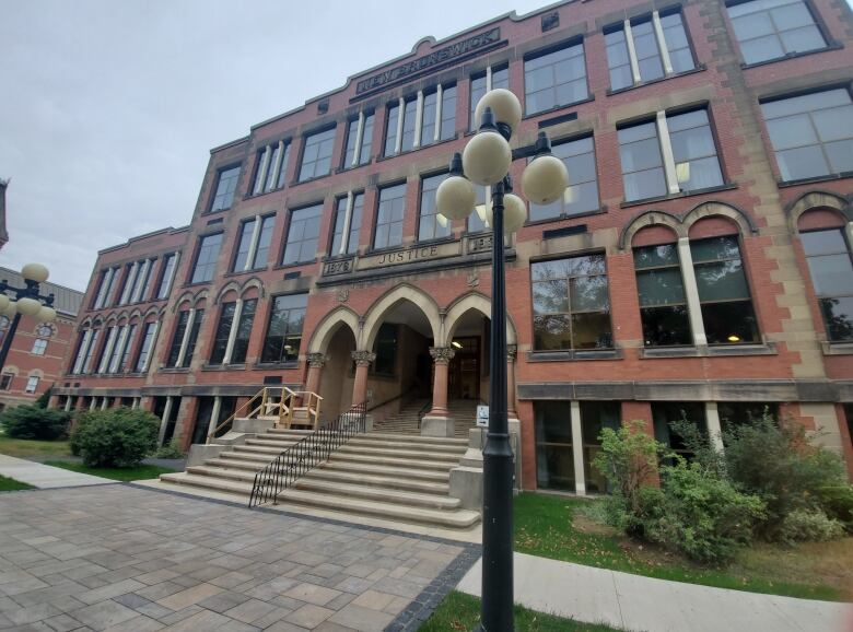 A brick building with the words Justice engraved at the top is shown, in front of a lamppost.