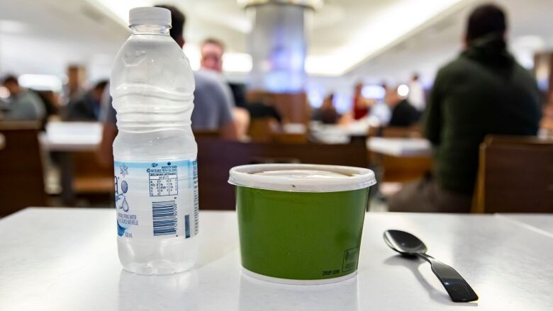 A plastic water bottle, green container and spoon rest on a table.