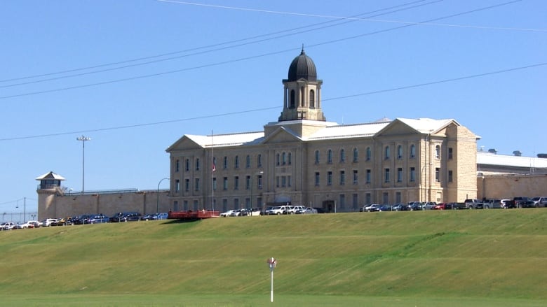 A large brick building with a bell tower is seen on a sunny day.