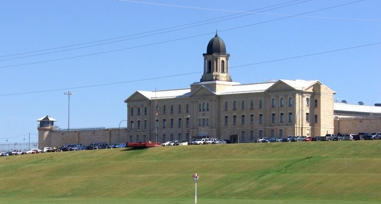 A large brick building with a bell tower is seen on a sunny day.