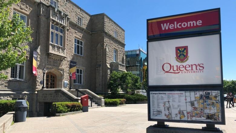 Exterior photo of a Queen's University sign with a campus building in the background