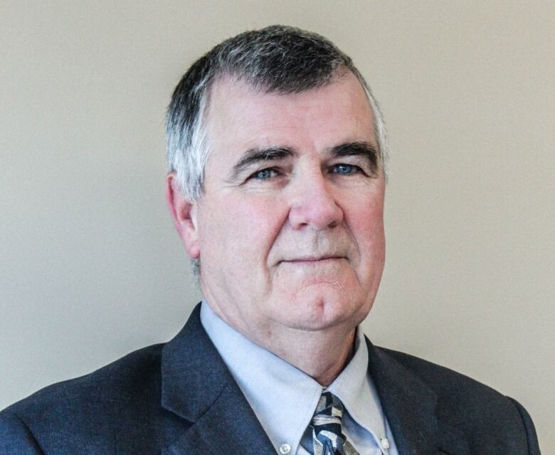 A man wearing a suit in front of a beige background