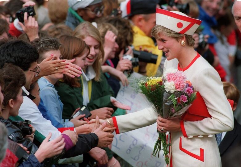 Woman holding bouquets shakes hands with members of a crowd