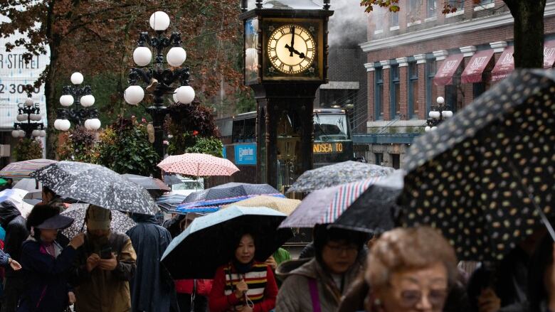 People carrying umbrellas walk near the steam clock in Vancouver's Gastown.