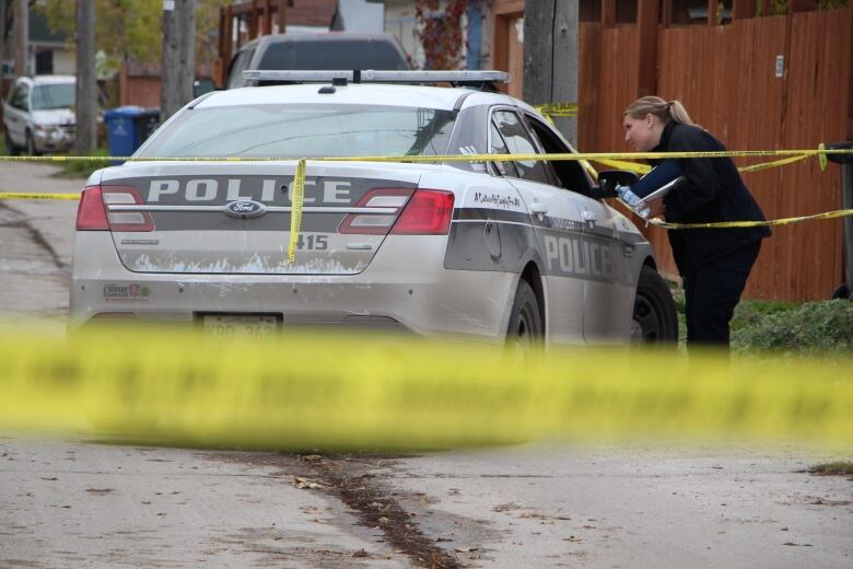 A police car is parked in an alley and surrounded by yellow police tape