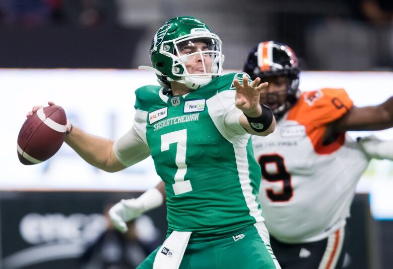 Football player looks to pass the football while defenders rush at him.