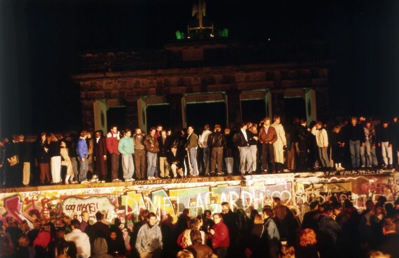 People stand on a cement wall covered in graffiti at night