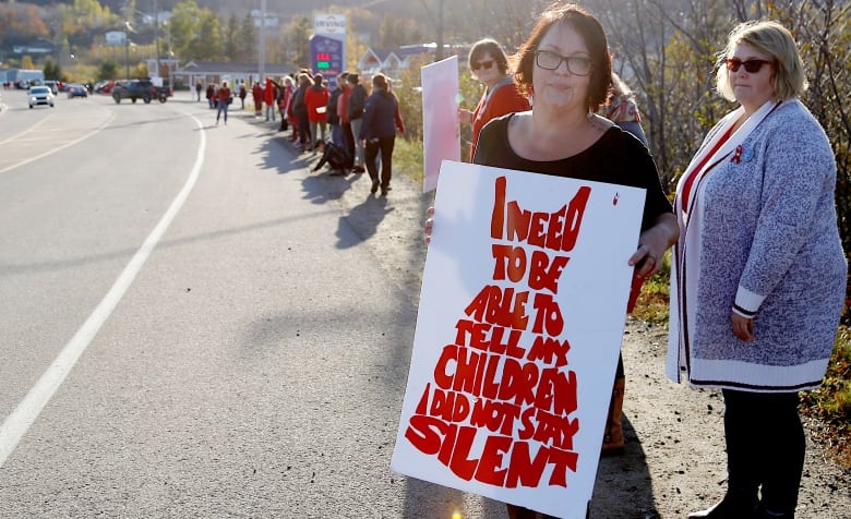 An Indigenous woman hold up a sign reading I need to be able to tell my children I did not stay silent.