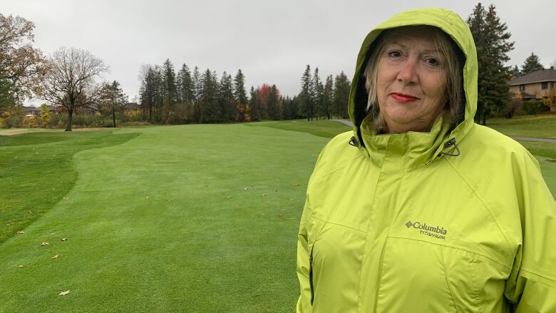 A woman in a bright green rainjacket stands on a golf course