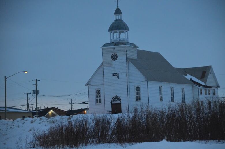 A large wooden church at twilight in the winter time.  