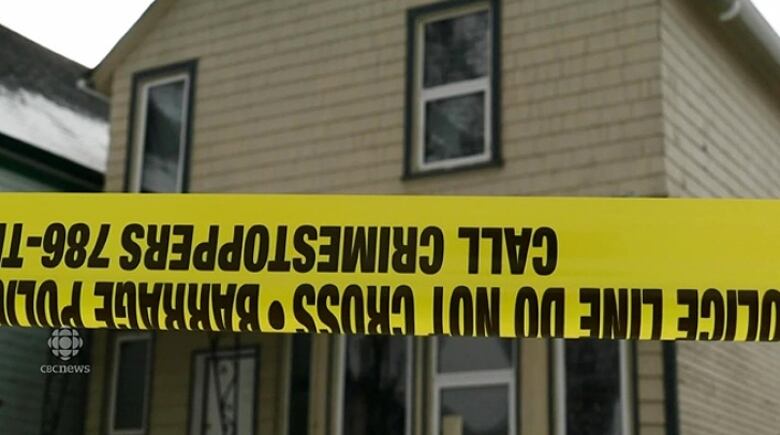 A house is seen behind yellow police tape.