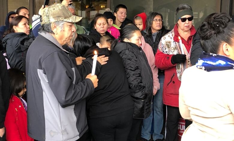 A group of people stands, some hugging, others holding candles.