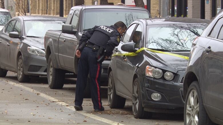 A police officer looks in the window of a car with police tape around it.