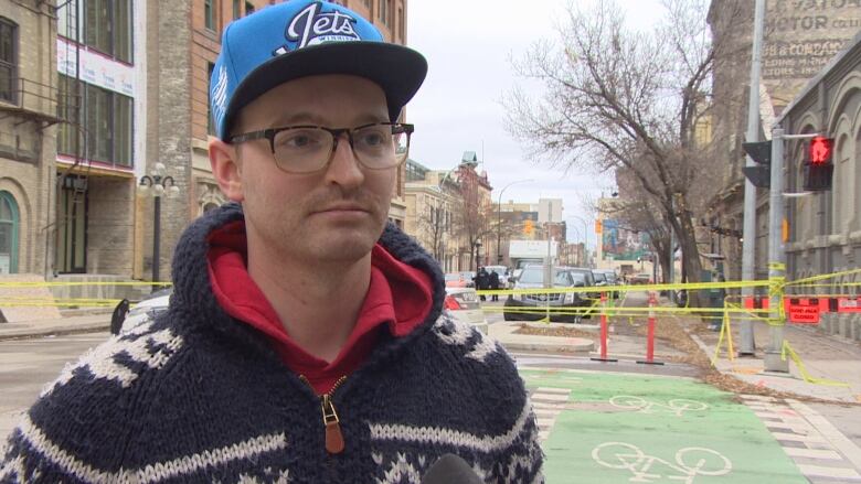 A man looks to the right of the camera. He stands in front of a street blocked with yellow police tape.