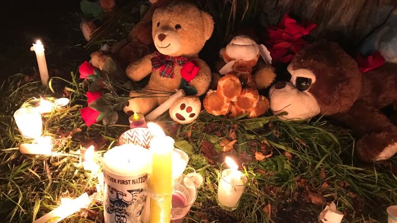 A pile of stuffed animals sits next to burning candles.