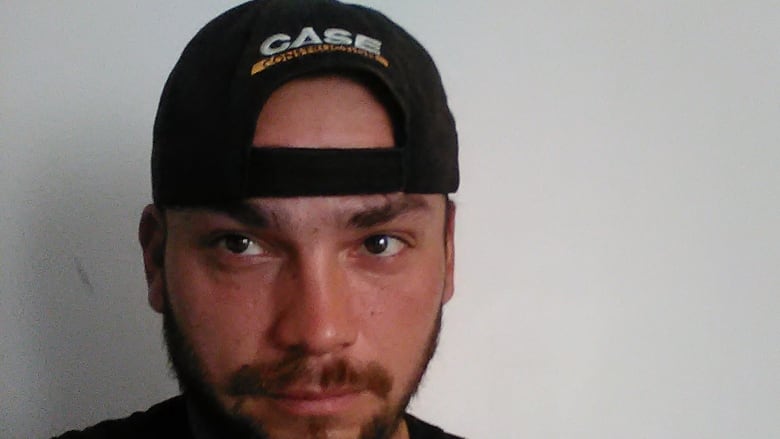 A man wearing a backwards baseball cap looks at the camera.