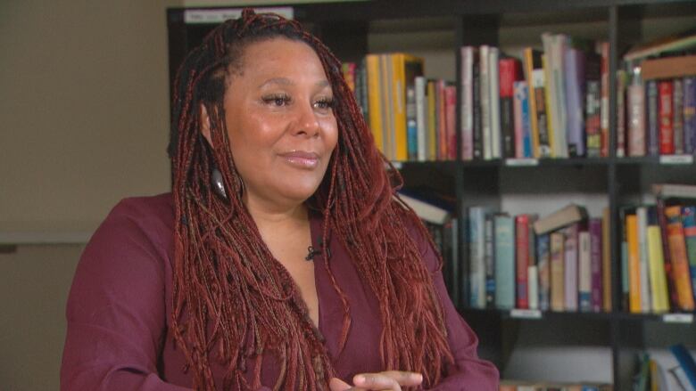 A Black woman with red braids sits in front of a bookcase.