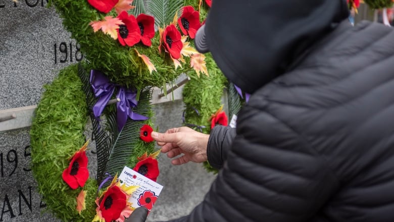 A member of the public pins a poppy to a wreath.