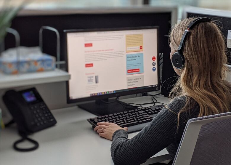 A woman typing at a computer with headphones on. 