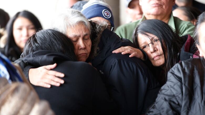 Women standing in a crowd embrace one another.