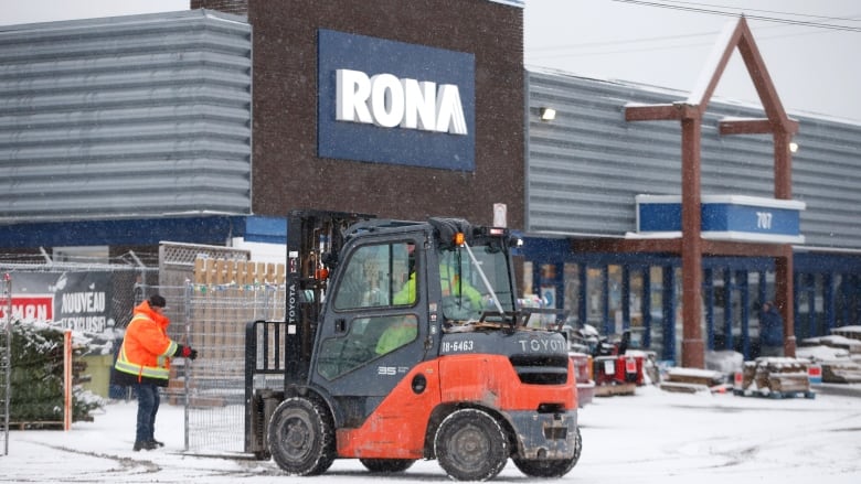 A Rona store is pictured in the winter, with a motorized vehicle lifting a pallet in front of the store.