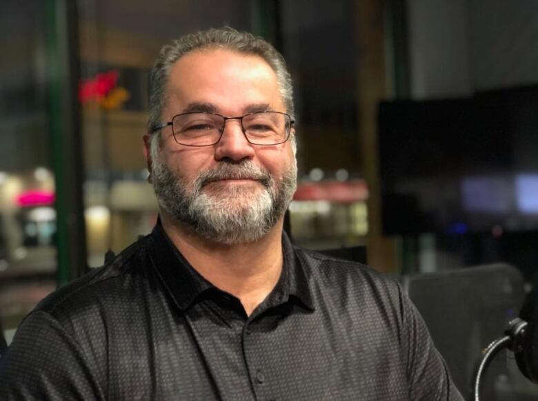 A man with a grey beard and glasses smiles.