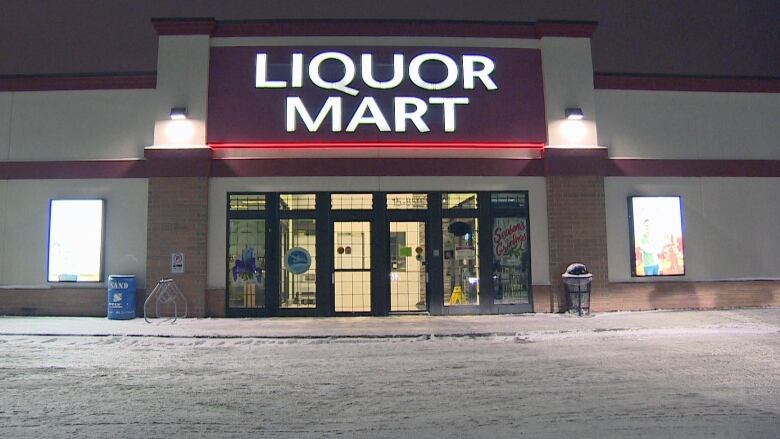 Photo shows an empty Liquor Marts building at night in winter with the lights on. 