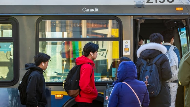 People enter a bus while wearing jackets and outerwear.