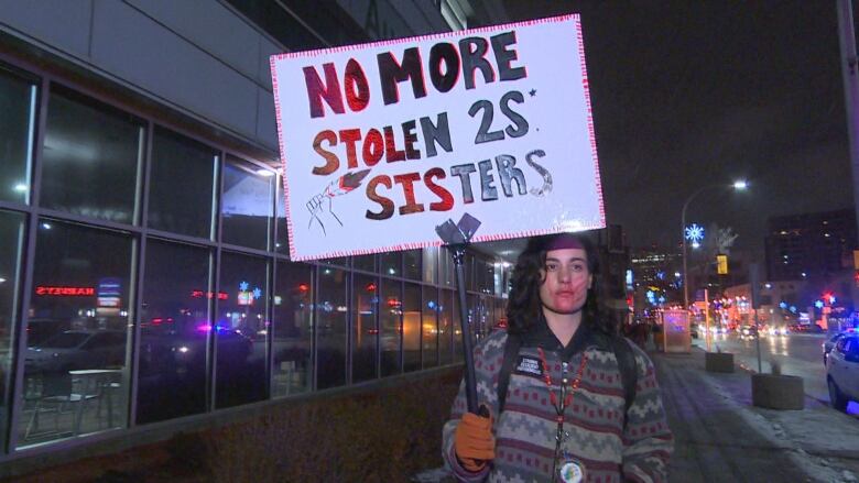 A woman with a red handprint on her lower face holds a sign that says 