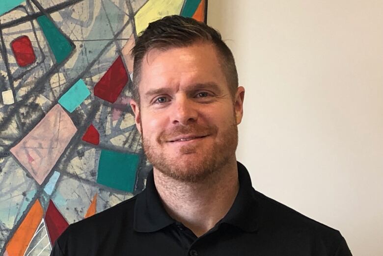 A grinning man standing in front of an abstract painting