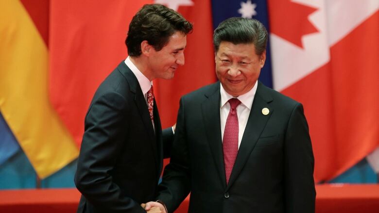 Two dark-haired men in suits exchange a close handshake.