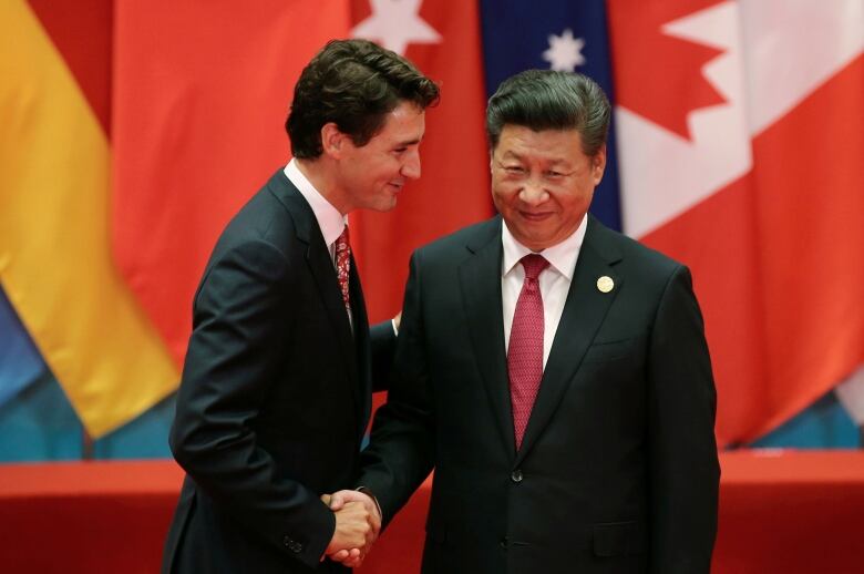 Two dark-haired men in suits exchange a close handshake.