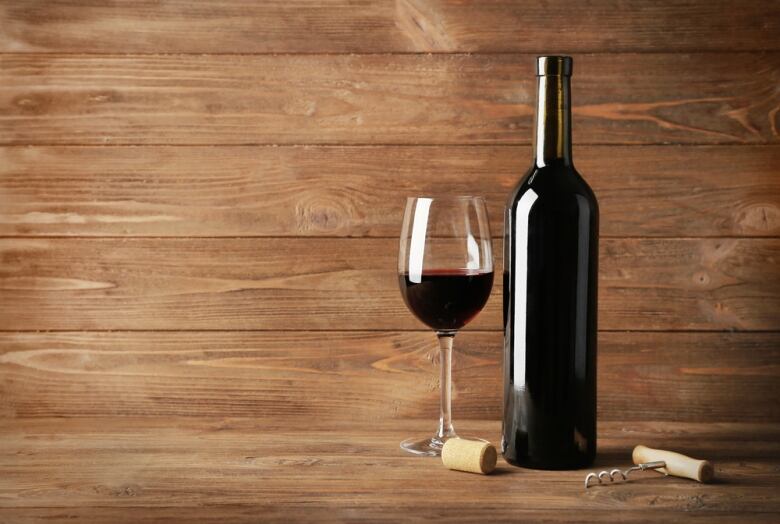 A glass of red wine sits next to an open bottle. 