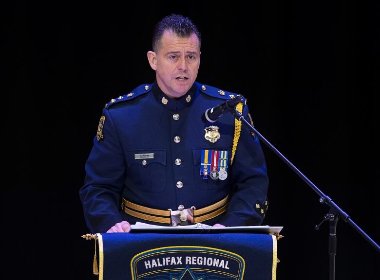 A White man is seen at a podium wearing high decorated police wear