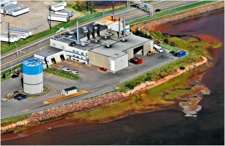 Aerial view of a large, industrial building on the edge of the water with smokestacks.